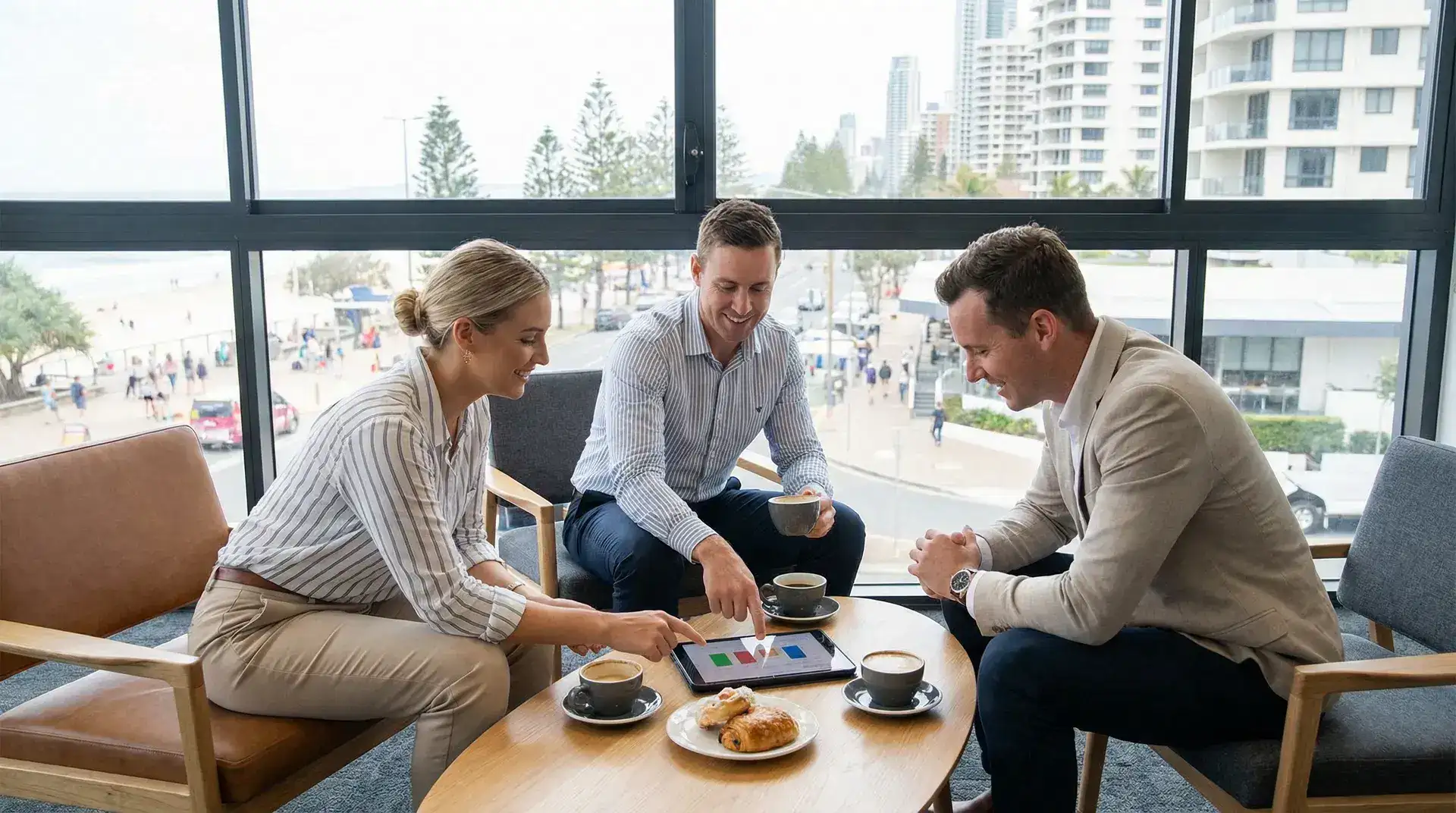 A casual business meeting in a Gold Coast cafe or modern office lounge, discussing technology plans on a tablet