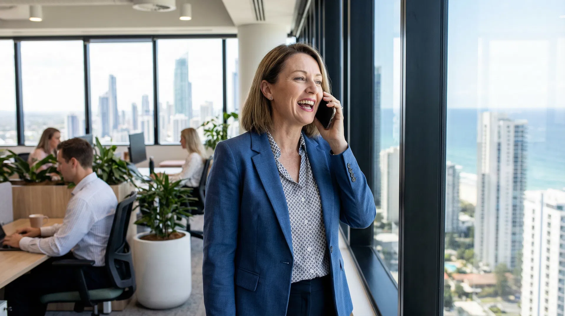 A relieved office manager in a modern Gold Coast office smiling while talking on the phone with IT support